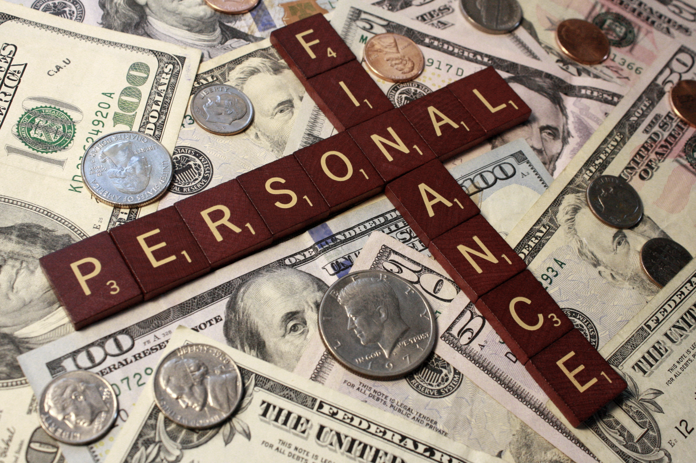 Scrabble tiles criss-cross and read "Personal Finance" and are laying on top of U.S. money. Personal finance blog concept.