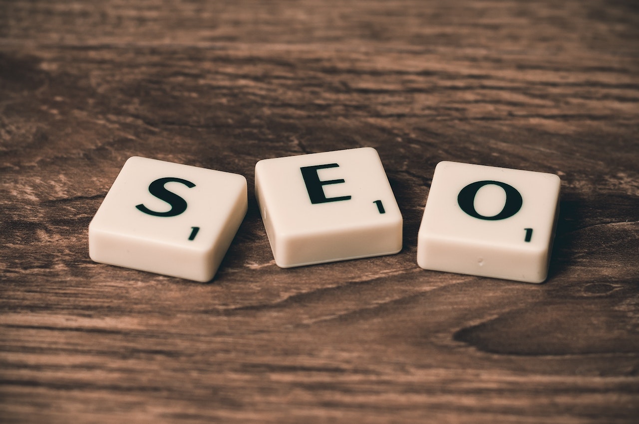 Three white Scrabble tiles read "SEO" against a brown table backdrop. Blog SEO concept. Photo by Pixabay.