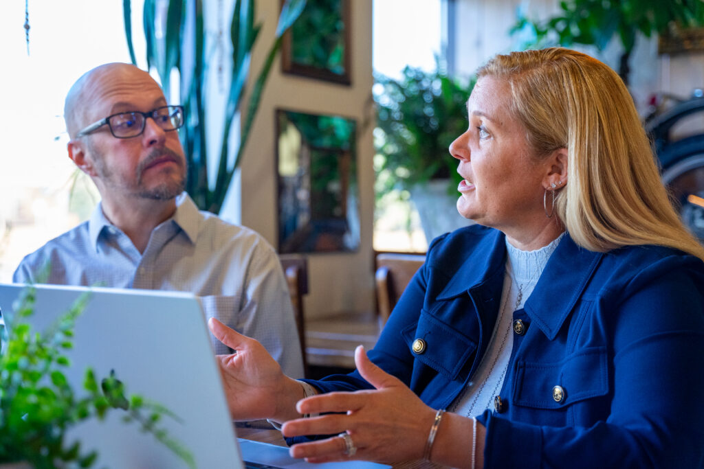 Image depicts two business partners having a conversation with a laptop on the table in front of them.